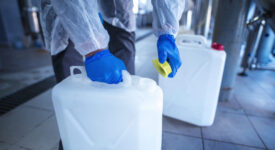 Unrecognizable person technologist in white protective suit handling acid or detergent in chemical industry. Industrial worker opening plastic canister to use chemicals.