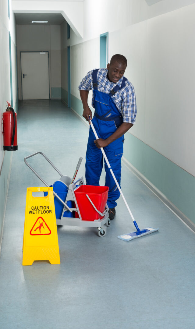 Portrait Of Young African Male Janitor Cleaning Floor In Corridor