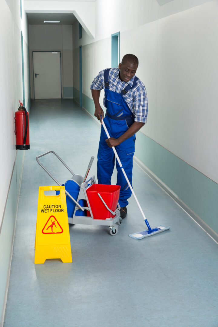 Portrait Of Young African Male Janitor Cleaning Floor In Corridor