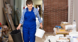 Young friendly  positive female worker holding buckets during doing finishing work in room