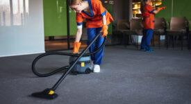 Smiling young female worker in the uniform leaning over a corded bagless canister vacuum cleaner