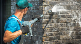 House Brick Wall Washing Using Pressure Washer. Caucasian Worker in His 30s.