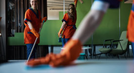 Smiling cute cleaner with a mop in her hands posing for the camera in the presence of her busy colleagues