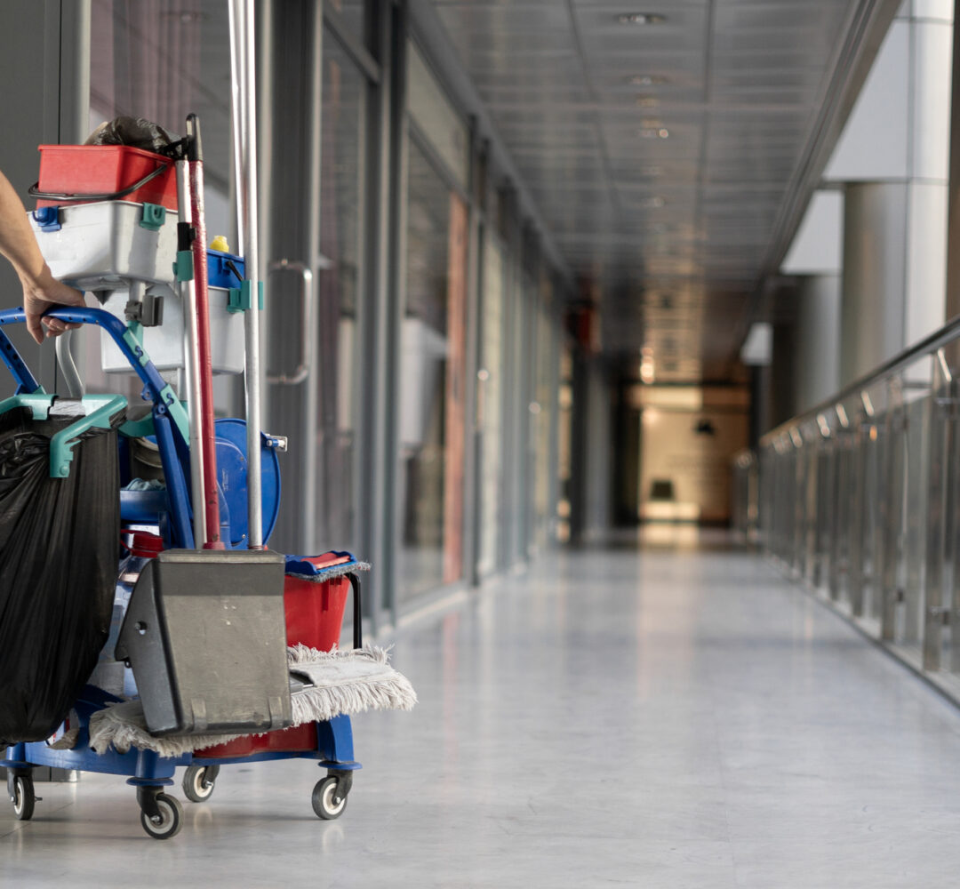 An employee pulls a trolley for cleaning offices. Woman cleaner is engaged in work. Shopping center place for text