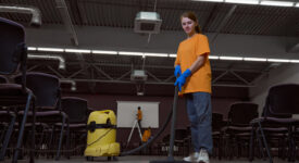 Full-size photo of focused young janitor vacuum-cleaning the floor in the conference hall
