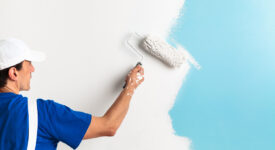 Back view of painter painting a wall with paint roller, with copy space